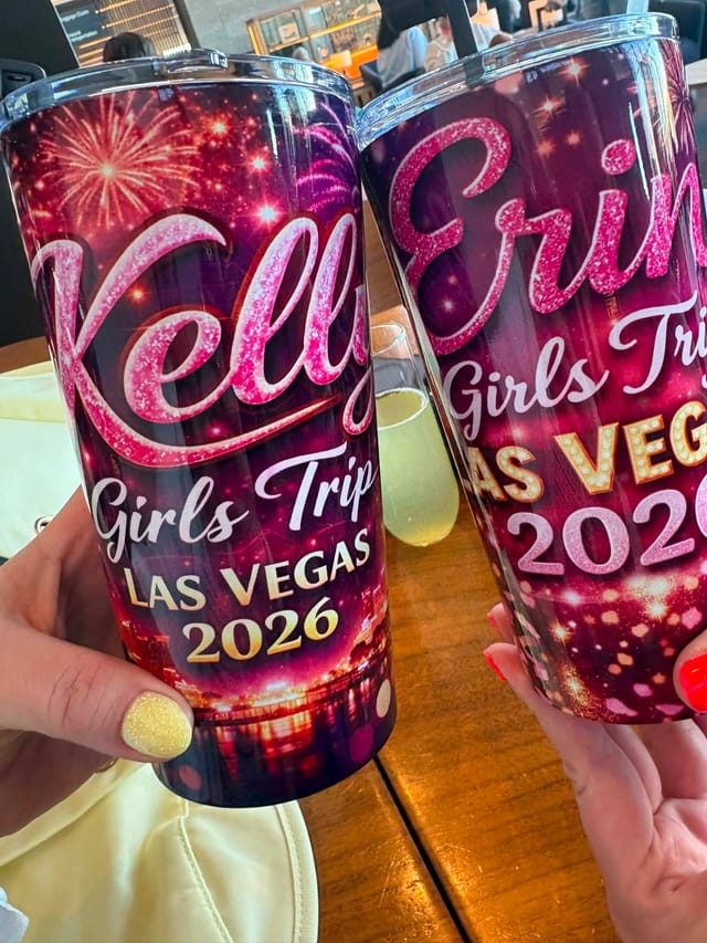 Two personalized glitter tumblers from a Las Vegas girls' trip, held up over a restaurant table